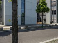 an empty sidewalk next to a tall building on a city street with no cars and a man sitting in a chair