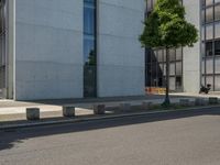 an empty sidewalk next to a tall building on a city street with no cars and a man sitting in a chair