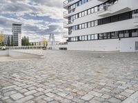 an empty sidewalk in front of two tall buildings with clouds overhead and some building blocks