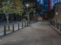 a very empty sidewalk in the evening with trees and buildings in the background during the day