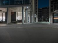 an empty sidewalk next to a glassy building at night with no one on it