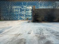 the view of an empty sidewalk in front of a tall building with blue glass on its side