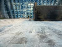 the view of an empty sidewalk in front of a tall building with blue glass on its side