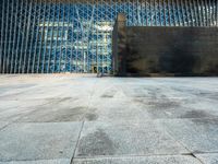 the view of an empty sidewalk in front of a tall building with blue glass on its side