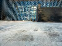 the view of an empty sidewalk in front of a tall building with blue glass on its side