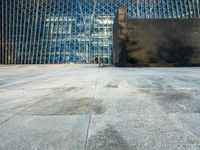 the view of an empty sidewalk in front of a tall building with blue glass on its side