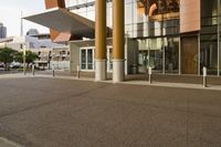 the sidewalk is empty with no cars in it near the building with many windows and pillars