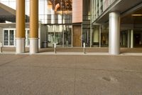 the sidewalk is empty with no cars in it near the building with many windows and pillars