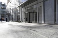 an empty sidewalk outside a large building with doors and people walking in it next to a glass door