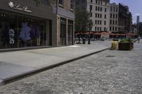 there is an empty sidewalk on the street with people walking on it and a store window on the corner