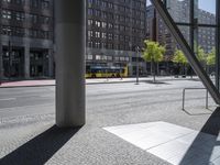 an empty sidewalk in front of tall buildings and a glass enclosure in the background is a brick walkway and a bench on the sidewalk