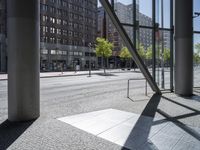 an empty sidewalk in front of tall buildings and a glass enclosure in the background is a brick walkway and a bench on the sidewalk