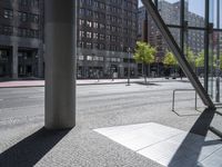 an empty sidewalk in front of tall buildings and a glass enclosure in the background is a brick walkway and a bench on the sidewalk