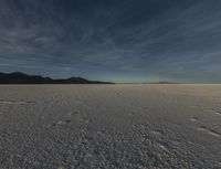 the snow covered field is empty but not far from the sun set, and has a lone figure standing on it