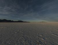 the snow covered field is empty but not far from the sun set, and has a lone figure standing on it