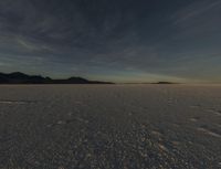 the snow covered field is empty but not far from the sun set, and has a lone figure standing on it