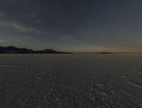 the snow covered field is empty but not far from the sun set, and has a lone figure standing on it