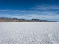 a large empty flat field of snow in the mountains, with mountains in the distance