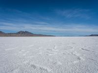 a large empty flat field of snow in the mountains, with mountains in the distance