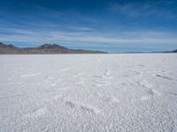 a large empty flat field of snow in the mountains, with mountains in the distance