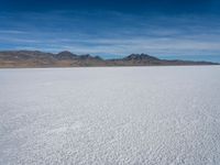 a large empty flat field of snow in the mountains, with mountains in the distance