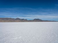 a large empty flat field of snow in the mountains, with mountains in the distance