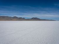 a large empty flat field of snow in the mountains, with mountains in the distance