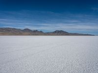 a large empty flat field of snow in the mountains, with mountains in the distance