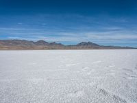 a large empty flat field of snow in the mountains, with mountains in the distance