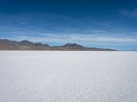 a large empty flat field of snow in the mountains, with mountains in the distance