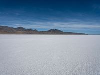 a large empty flat field of snow in the mountains, with mountains in the distance