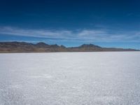 a large empty flat field of snow in the mountains, with mountains in the distance