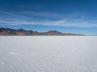 a large empty flat field of snow in the mountains, with mountains in the distance