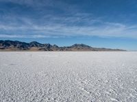 a large empty flat field of snow in the mountains, with mountains in the distance