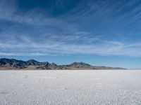 a large empty flat field of snow in the mountains, with mountains in the distance