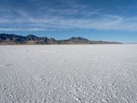 a large empty flat field of snow in the mountains, with mountains in the distance