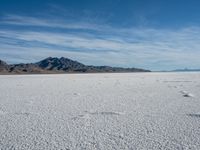 a large empty flat field of snow in the mountains, with mountains in the distance