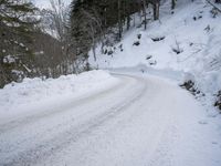 an empty snowy mountain road near mountains and trees with snow piled up on the sides