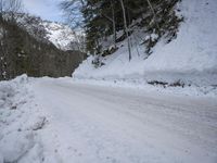 an empty snowy mountain road near mountains and trees with snow piled up on the sides