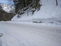 an empty snowy mountain road near mountains and trees with snow piled up on the sides