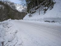 an empty snowy mountain road near mountains and trees with snow piled up on the sides