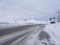 an empty snowy road with a sign showing directions at the corner and mountains in the background