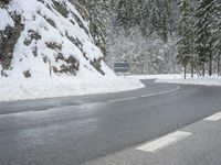 the road is very slippery and empty on a snowy day near a pine tree lined mountain