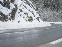 the road is very slippery and empty on a snowy day near a pine tree lined mountain