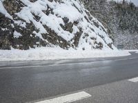 the road is very slippery and empty on a snowy day near a pine tree lined mountain