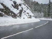 the road is very slippery and empty on a snowy day near a pine tree lined mountain