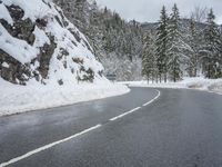 the road is very slippery and empty on a snowy day near a pine tree lined mountain