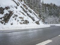 the road is very slippery and empty on a snowy day near a pine tree lined mountain