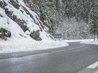 the road is very slippery and empty on a snowy day near a pine tree lined mountain