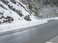 the road is very slippery and empty on a snowy day near a pine tree lined mountain